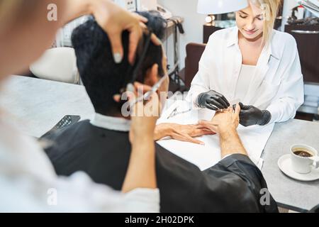 Client getting nails polished during haircut in beauty salon Stock Photo