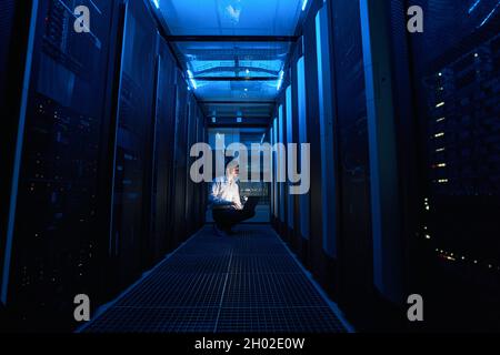 Technician looking at server cabinet while using laptop Stock Photo