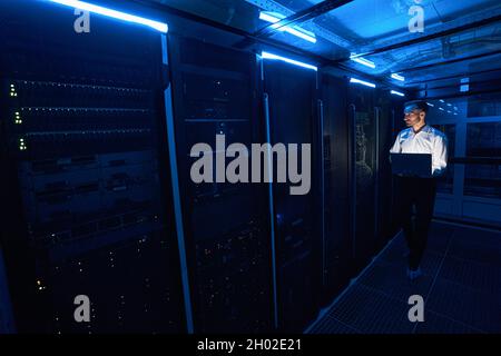 Male server technician walking with laptop in data center room Stock Photo