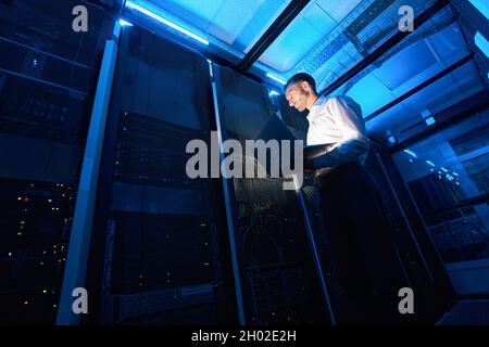 Network administrator using laptop while doing computer equipment checkup Stock Photo