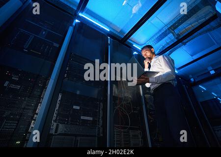 IT technician analyzing data from laptop in server room Stock Photo