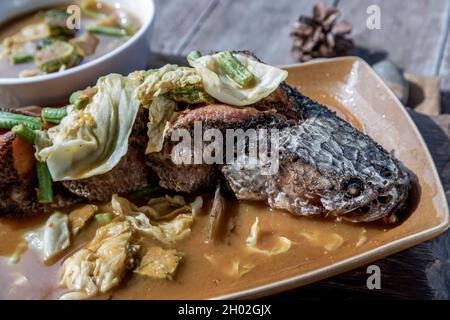 Deep fried whole Snakehad fish topped with Acacia omelets in vegetable sour soup (Orange curry with Cha-om). Stock Photo