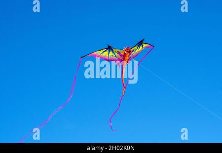 A dragon kite flies in the wind in a clear blue sky Stock Photo