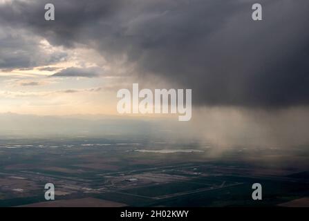rain and storm clouds pour down over a city while viewed from the window of an airplane Stock Photo