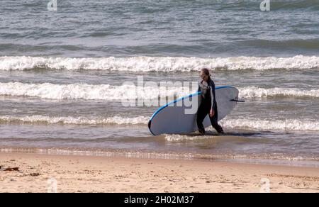 St Joseph MI USA, Sept 26, 2021; a woman in a wet suit walked out of a cold Lake Michigan, with her surf board Stock Photo