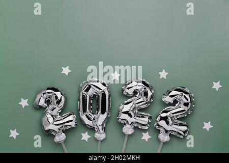 New Year 2022 or Christmas green background flat lay. Top view on 2022 balloon silver or metallic numbers on sticks with stars. Invitation or greeting Stock Photo