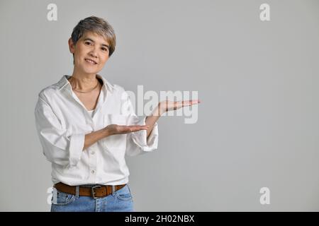 Middle aged Asian woman showing empty copy space on the open hands palm for text or product isolated on white background. looking at the camera Stock Photo