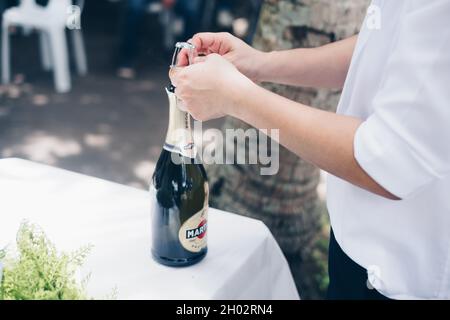 NORALA, PH– SEPT 22, 2021: Hands opening the Martini sparkling wine bottle on a white table. Selective focus. Copy space. Stock Photo