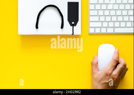 Hand holding wireless mouse with keyboard for online shopping on yellow background. Cyber Monday and Black Friday concept. Stock Photo