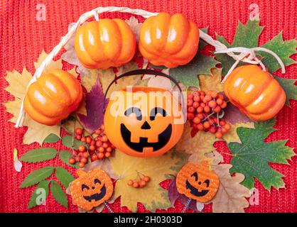 Halloween Jack o Lantern with sweets on a colorful autumn background from dried leaves and orange rowan berries on a knitted red background. Bright au Stock Photo