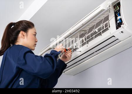 female technician service using screwdriver to repairing the air conditioner indoors Stock Photo