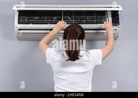 young woman removing air filter of the air conditioner for cleaning at home Stock Photo