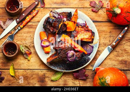 Baked beef ribs with pumpkin on wooden table.Roasted veal meat with slices of pumpkin Stock Photo