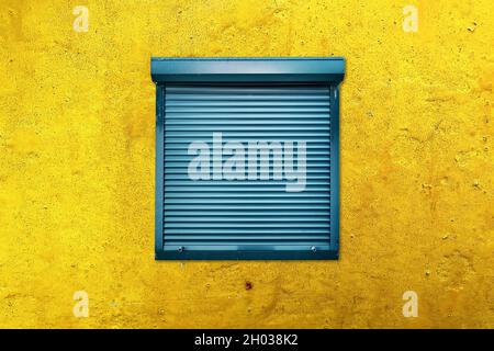 Square window with closed blue blinds or rolling shutter on a yellow weathered wall. Secrecy, mystery or protection concept. Stock Photo
