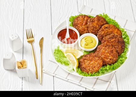 baked pork patties with cheese crust on a green lettuce lives with ketchup and mustard on a plate Stock Photo