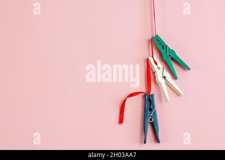Sewing tape and three plastic clothespins against a pink background. The clothespins hang vertically on a thin red ribbon. Selective Focus. Stock Photo