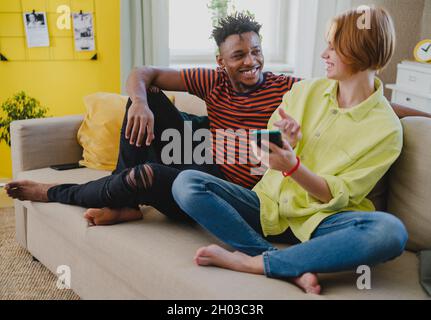 Young biracial couple using smartphone, having fun at home, checking social networks together. Stock Photo