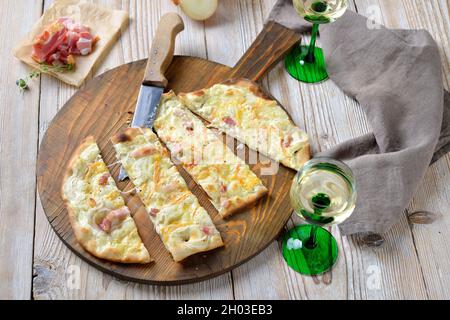 Hearty tarte flambée from Alsace with onions, smoked bacon and munster cheese hot from the oven, served with Alsatian white wine Stock Photo