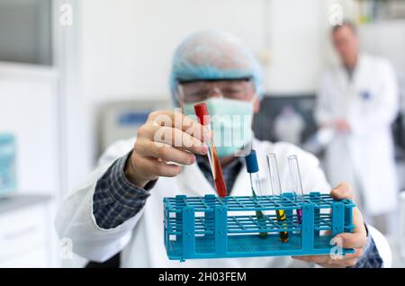 Close up of researcher's hand holding test tubes with colorful liquids in laboratory Stock Photo