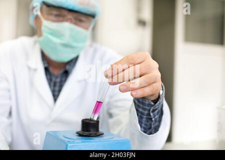 Close up of researcher's hand holding test tube with fluid above vibrator in laboratory Stock Photo