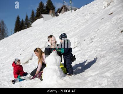 Parents with two boys playing on snow, making snowman. Winter family vacation Stock Photo