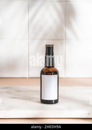 Amber bottle with white label mockup for bathing products in bathroom on marble table and white wall tile. Palm leaf shadow. Front view. Copy space Stock Photo