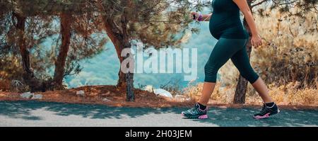 Sportive Pregnant Woman Jogging in the Mountainous Forest in Sunny Day. Enjoying the Walk Among Fresh Pine Trees. Body Part. Healthy Pregnancy. Stock Photo