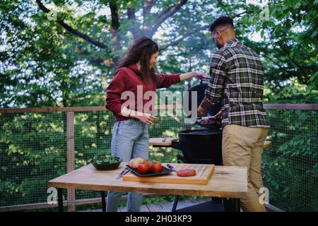 Happy biracial couple resting and preparing burgers outdoors in a tree house, weekend away and digital detox concept. Stock Photo