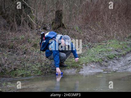 Man picking water from river for drinking in forest in winter Stock Photo