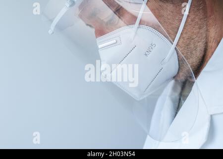 Medical professional wearing visor and KN95 respiratory mask during Covid-19 pandemics, sad and tired doctor in hospital Stock Photo