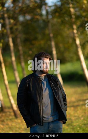 Young bearded man standing and looking at distance against a background of colorful autumn trees Stock Photo