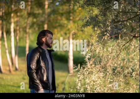 Side view of a young thoughtful bearded man in a black leather jacket, outdoor portrait Stock Photo