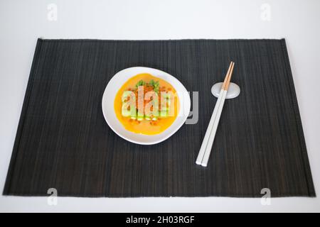 Mini asparagus with sauce and red caviar on white plate with chopsticks on black mat in Japanese restaurant, close up, flat lay, picture for the menu Stock Photo