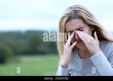 Teen scratching itchy eyes with both hands outdoors in a field Stock Photo