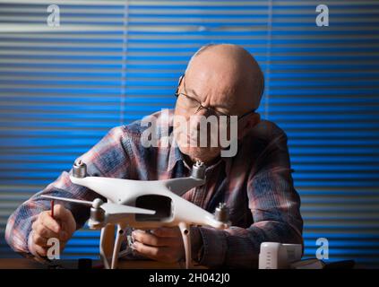 Old man repairing drone with screwdriver on desk in the office Stock Photo
