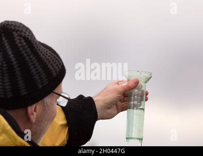 Senior farmer holding rain gauge high in sky in field Stock Photo