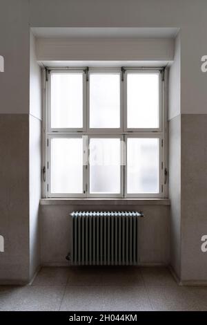 Old metallic water heater radiator mounted beneath a large window Stock Photo