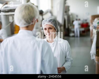 Two female workers discussing about food quality while standing in food factory. Stock Photo