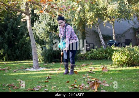 Pretty young woman using leaf blower for seasonal works in backyard Stock Photo