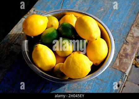 lemons and limes in metal bowl on blue painted weathered table top Stock Photo