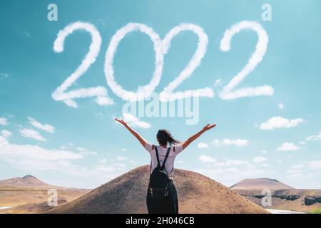 Brunette woman greets the 2022 against clouds .