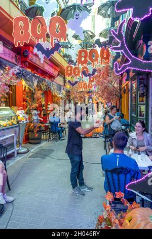 Athens  Greece - 10.10.202: People sitting outside in a street cafe at Halloween. The alley is fully decorated with scary and funny holiday objects. Stock Photo