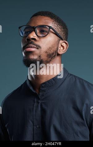 Minimal vertical portrait of handsome African-American man wearing glasses and looking away while posing against deep blue background Stock Photo