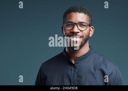 Portrait of handsome African-American man wearing glasses and looking at camera smiling while posing against deep blue background, copy space Stock Photo