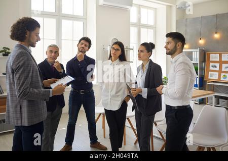 Young man shares his business ideas with colleagues standing next to him in a modern bright office. Stock Photo