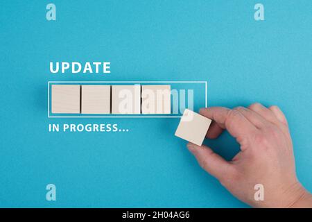 The words update in progress are standing beside the loading bar, hand puts last cube to the upload, blue colored background Stock Photo