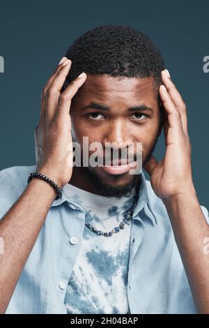 Vertical portrait of handsome African-American young man looking at camera smiling while posing against blue background Stock Photo