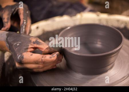 Womens hands at work on a potters wheel with black clay blank Stock Photo