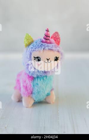 Colored plush llama unicorn on white wooden background. Famous and popular kids toy. Stock Photo