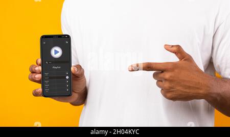 Unrecognizable Black Man Pointing At Music Player App Opened On Modern Smartphone, African American Male Recommending New Audio Streaming Application Stock Photo